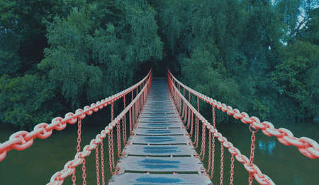 Red metal suspension bridge over the river in the park. High quality photoの写真素材