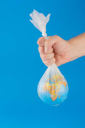 Hand holding planet earth inside a plastic bag over blue background