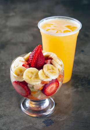 Fruit salad on a glass with orange juice over stone backgroundの写真素材