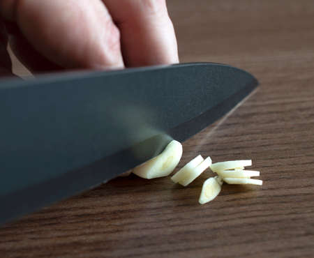 Garlic clove beeing sliced with dark gray knife over wood backgroundの写真素材