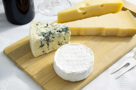 Parmesan, gorgonzola and camembert cheese over wood board beside wine bottle