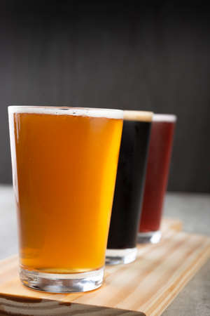 Three pint glasses of beer over wooden board. Golden, dark and red beerの写真素材