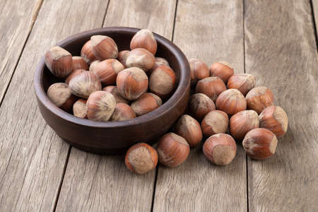 A group of hazelnuts in a bowl over wooden table.