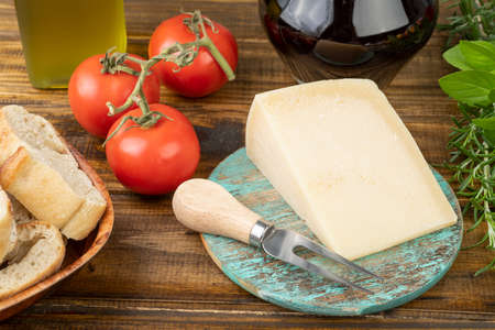 Parmesan cheese, tomatoes, olive oil, wine, bread and herbs over wooden table. Mediterranean food.