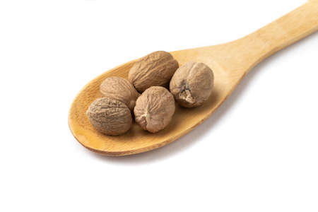 Closeup of nutmegs on a wooden spoon isolated over white background.