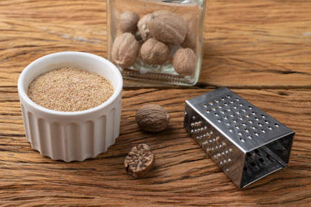 Nutmegs with grater over wodden table. Nutmeg powder in a bowl.の写真素材