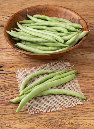 A group of green bean pods in a bowl over wooden table.