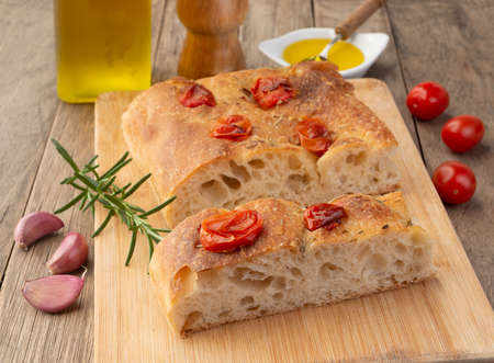 Homemade focaccia with cherry tomato, garlic, olive oil and rosemary over wooden table.の写真素材