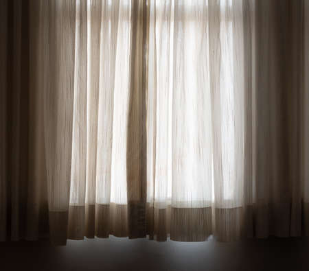 Light brown curtain in a dark room in front of the window.の写真素材
