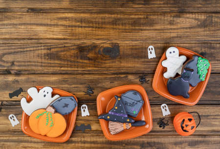 Halloween gingerbread cookies, pumpkin, tombstone, witch hat, black cat on plates over wooden table...