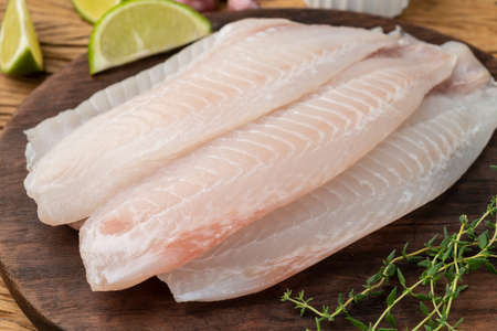 Raw tilapia fish fillet with seasonings over wooden table.