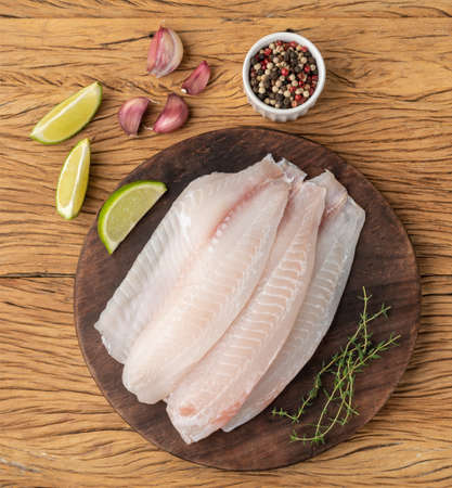 Raw tilapia fish fillet with seasonings over wooden table.