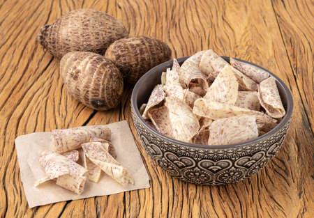 Yam or taro chips in a bowl with raw vegetable over wooden table.