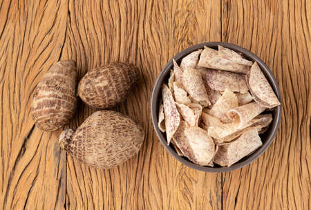 Yam or taro chips in a bowl with raw vegetable over wooden table.