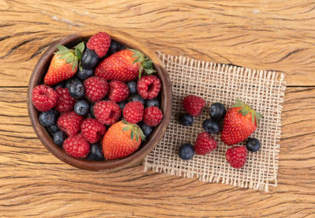 Raspberries, strawberries and blueberries in a bowl over wooden table.の写真素材