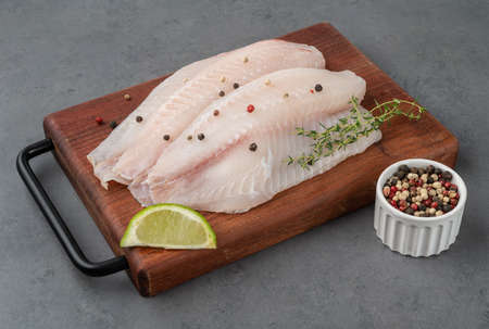 Raw tilapia fish fillet with seasonings over stone background.の写真素材