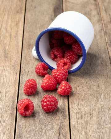 A group of raspberries on a cup over wooden table.