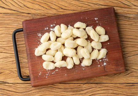 Uncooked italian pasta gnocchi on a board over wooden table.の写真素材