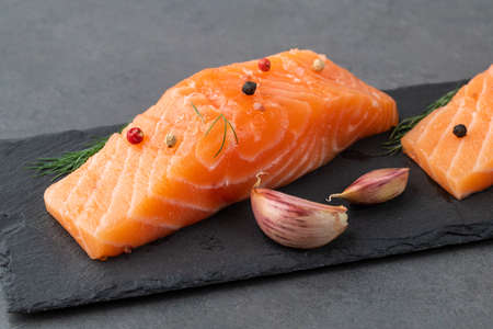 Raw salmon slices with seasonings over stone board.