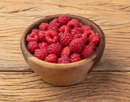 Raspberries in a bowl over wooden table.