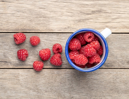 A group of raspberries on a cup over wooden table.