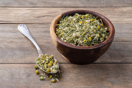 Chamomile dried tea leaves and flowers in a bowl over wooden table.の写真素材