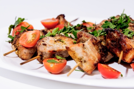 Barbecue on skewers, garnished with cherry om white plateの写真素材