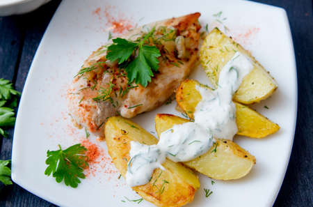 grilled chicken breast with roasted potatoes on white plateの写真素材