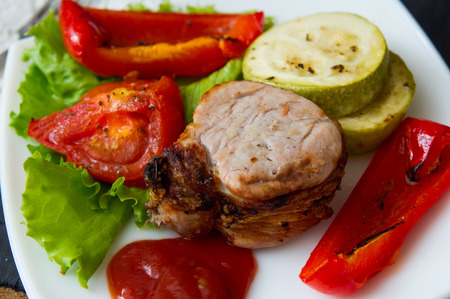 roasted pork steak with grilled vegetables on white plateの写真素材