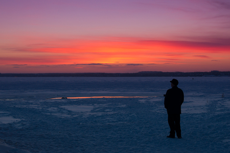 man watching the sunset on the shore of the winter lakeの写真素材