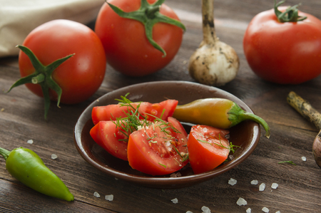 Ripe red sliced tomatoes, hot chili peppers, garlic on a wooden tableの写真素材