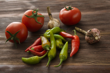 Ripe red tomatoes, hot chili peppers, garlic on a wooden tableの写真素材
