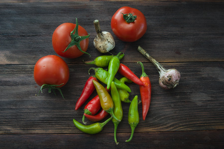 Ripe red tomatoes, hot chili peppers, garlic on a wooden tableの写真素材