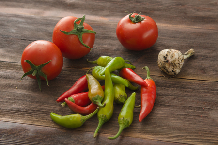 Ripe red tomatoes, hot chili peppers, garlic on a wooden tableの写真素材