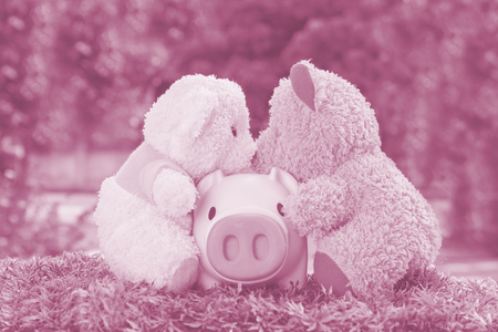 White and brown teddy bear with a pink pig on green grassの写真素材
