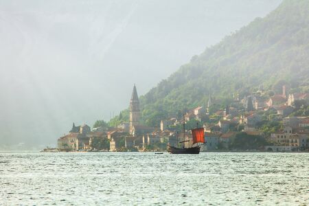 Old ship in the sea on old town and foggy moutainsの写真素材