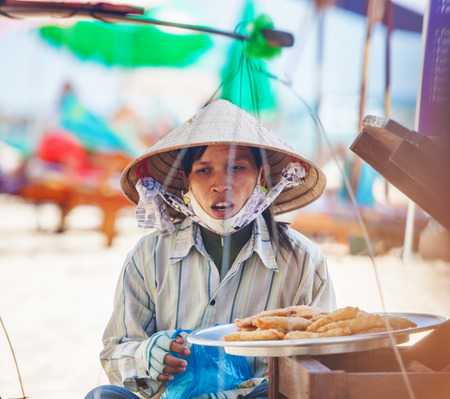 PHU QUOC, VIETNAM - APRIL 26, 2014  Vietnamese woman in traditional headdress, which protects from the sun offers fruits for sale to tourists at Long beach on Phu Quoc island, Vietnam  のeditorial素材