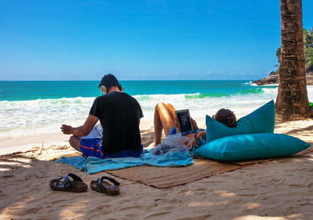 PHUKET, THAILAND- OCTOBER11, 2014: man listening music, woman using tablet on Surin beach. Surin is exclusive beach retreat for discerning travelers and couples seeking relaxation in a serene settingのeditorial素材