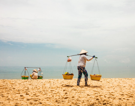 PHU QUOC, VIETNAM - APRIL 18, 2014: Vietnamese womans in traditional headdress, which protects from the sun offers fruits for sale to tourists at Long beach on Phu Quoc island, Vietnam.のeditorial素材