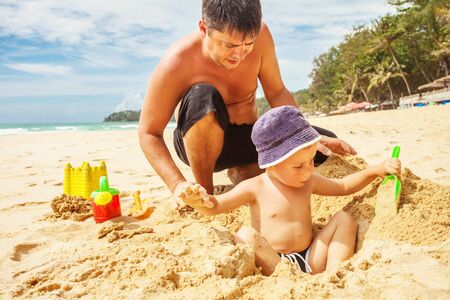 Boy and dad playing in the sand on the beachの写真素材