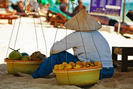 PHU QUOC, VIETNAM - APRIL 26, 2014: Vietnamese fruits saleswoman with traditional headdress, which protects from the sun, resting on in shadow of beach umbrella Long beach on Phu Quoc island, Vietnamのeditorial素材
