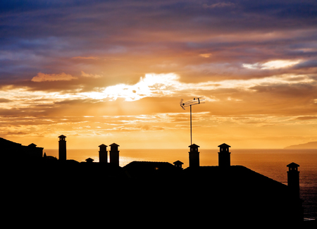 Sunset silhouettes of roofs of houses with chimneysの写真素材