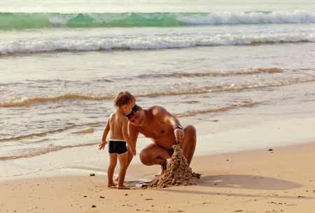 father and his little son building sand castle at beachの写真素材