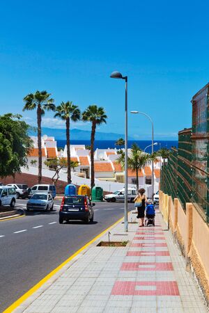 TENERIFE ISLAND, SPAIN - APRIL 10, 2017 : Street with cars, along the sidewalk there is a woman with a baby and a stroller in Costa Adeje, Tenerife, Canary Islandsのeditorial素材