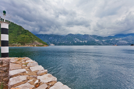 Small lighthouse at embankment overlooking the mountains in gloomy weather. Kotor bay. Montenegroの写真素材