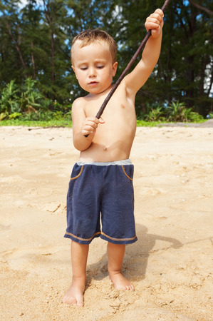 Little boy is playing with a wooden stick on a sandy beachの写真素材