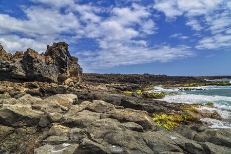 Wild stone beach on coast or shore of the Atlantic ocean with waves under blue sky. Tenerife island....
