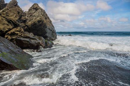 Close up shot how Atlantic ocean wave breaks on the big rocky stone on the beautiful Moinhos beach of Sao Miguel island of Azores, Portugalの写真素材
