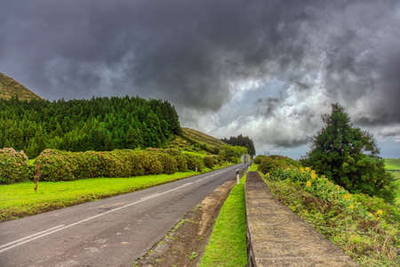 Road is leading through green hills landscape on the island of Sao Miguel, Azores, Portugalの写真素材