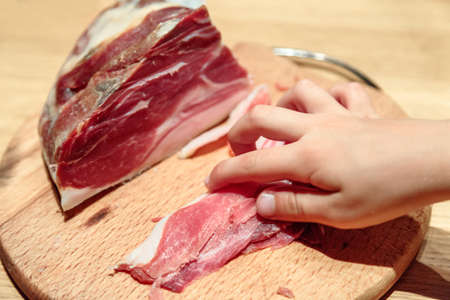 Boy hand taking sliced jamon (hamon) from a wooden board. Selective focusの写真素材